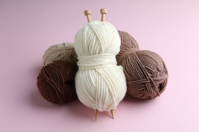 Skeins of yarn and knitting needles on pink background