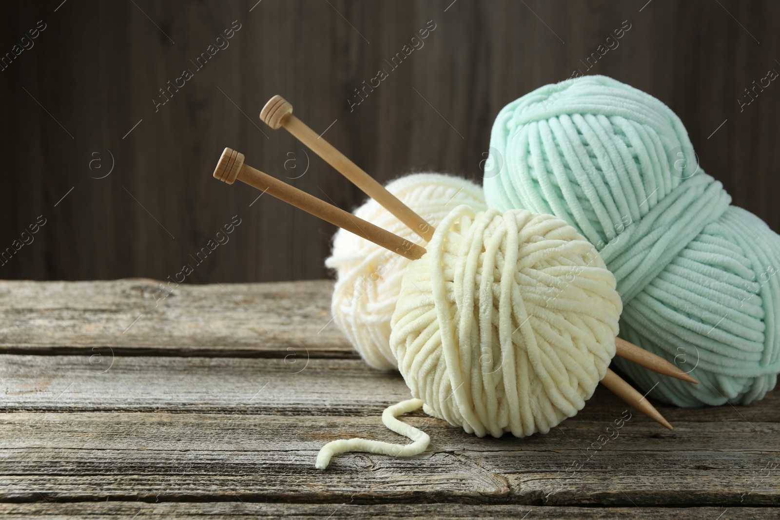 Photo of Skeins of yarn and knitting needles on wooden table, closeup. Space for text