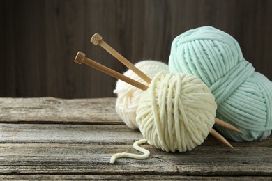 Skeins of yarn and knitting needles on wooden table, closeup. Space for text