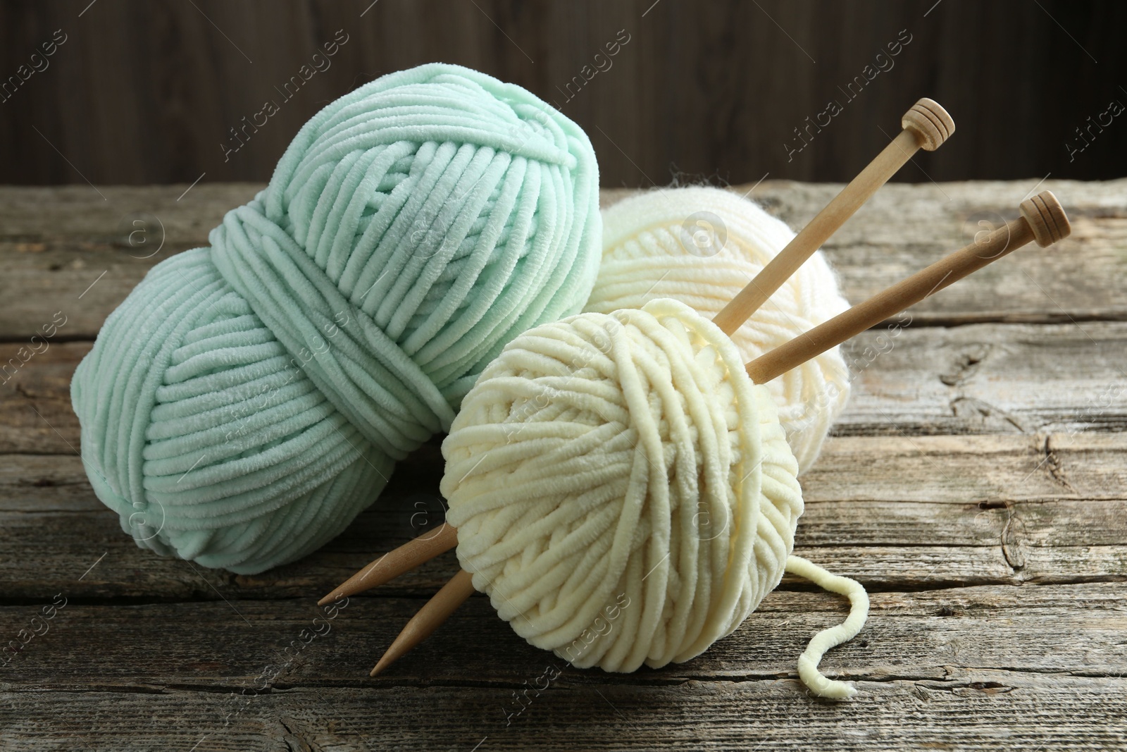 Photo of Skeins of yarn and knitting needles on wooden table, closeup