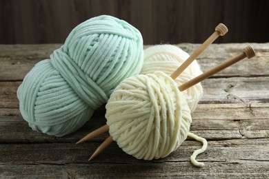 Photo of Skeins of yarn and knitting needles on wooden table, closeup