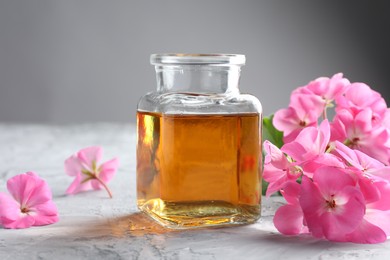 Photo of Bottle of geranium essential oil and beautiful flowers on light grey textured table, closeup