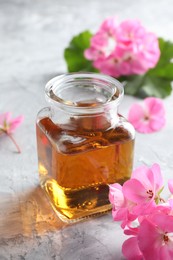 Photo of Bottle of geranium essential oil and beautiful flowers on light grey textured table, closeup