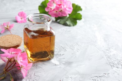 Photo of Bottle of geranium essential oil and beautiful flowers on light grey textured table