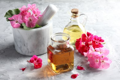 Photo of Geranium essential oil and beautiful flowers on light grey textured table