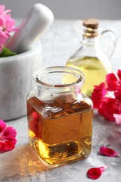 Photo of Geranium essential oil and beautiful flowers on light grey textured table, closeup