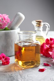 Photo of Geranium essential oil and beautiful flowers on light grey textured table