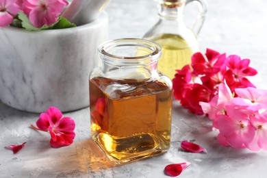 Photo of Geranium essential oil and beautiful flowers on light grey textured table, closeup