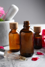 Photo of Geranium essential oil in bottles, pipette and petals on light grey textured table