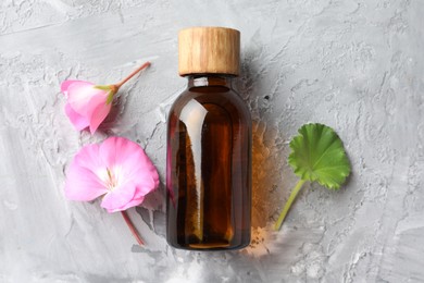 Photo of Bottle of geranium essential oil and beautiful flowers on light grey textured table, flat lay