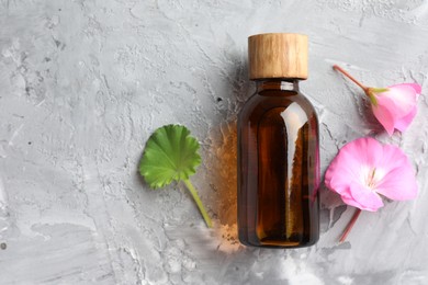 Photo of Bottle of geranium essential oil and beautiful flowers on light grey textured table, flat lay. Space for text