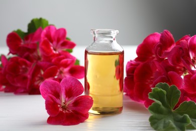 Photo of Bottle of geranium essential oil and beautiful flowers on white wooden table, closeup