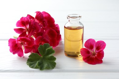 Photo of Bottle of geranium essential oil and beautiful flowers on white wooden table, closeup