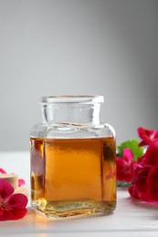 Photo of Bottle of geranium essential oil and beautiful flowers on white wooden table, closeup