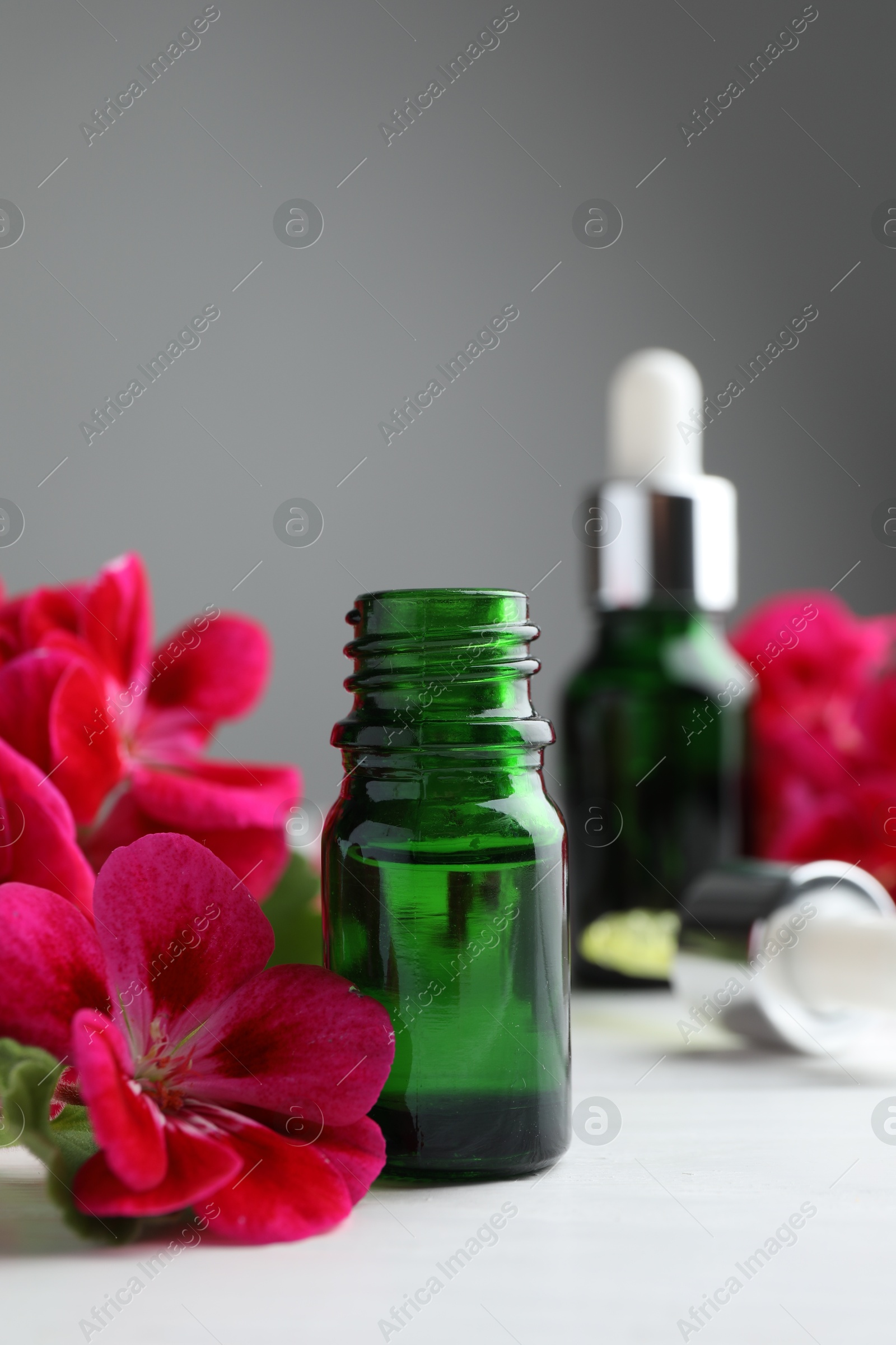 Photo of Bottles of geranium essential oil and beautiful flowers on white wooden table, closeup