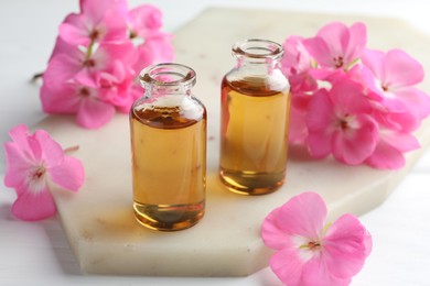 Photo of Bottles of geranium essential oil and beautiful flowers on white table, closeup