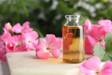 Photo of Bottle of geranium essential oil and beautiful flowers on white table, closeup