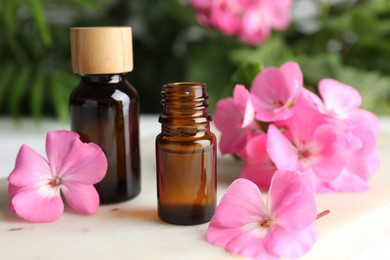 Photo of Bottle of geranium essential oil and beautiful flowers on white table, closeup