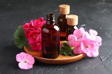 Photo of Bottles of geranium essential oil and beautiful flowers on black table, closeup