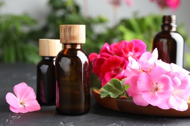 Photo of Bottles of geranium essential oil and beautiful flowers on black table, closeup