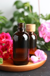 Photo of Bottles of geranium essential oil and beautiful flowers on black table, closeup