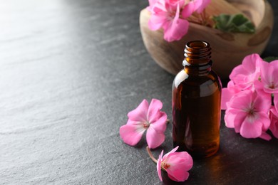 Photo of Bottle of geranium essential oil and beautiful flowers on black table, closeup. Space for text