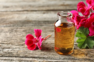 Photo of Bottle of geranium essential oil and beautiful flowers on wooden table, closeup. Space for text