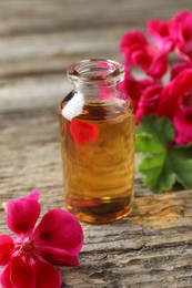 Photo of Bottle of geranium essential oil and beautiful flowers on wooden table, closeup