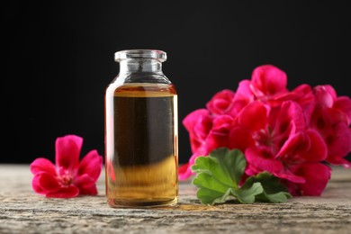 Photo of Bottle of geranium essential oil and beautiful flowers on wooden table, closeup