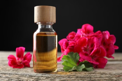 Photo of Bottle of geranium essential oil and beautiful flowers on wooden table, closeup