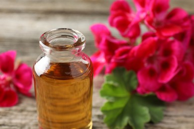 Photo of Bottle of geranium essential oil and beautiful flowers on table, closeup