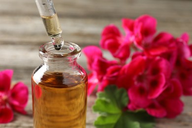 Photo of Geranium essential oil dripping from pipette into bottle on table, closeup