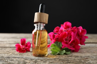 Photo of Bottle of geranium essential oil and beautiful flowers on wooden table, closeup