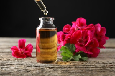 Photo of Geranium essential oil dripping from pipette into bottle on wooden table, closeup