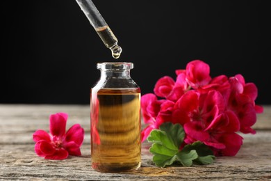 Geranium essential oil dripping from pipette into bottle on wooden table, closeup