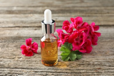 Photo of Bottle of geranium essential oil and beautiful flowers on wooden table