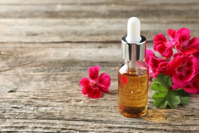 Photo of Bottle of geranium essential oil and beautiful flowers on wooden table. Space for text