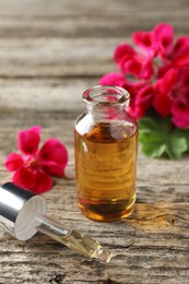 Photo of Bottle of geranium essential oil, pipette and beautiful flowers on wooden table