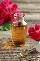 Photo of Bottle of geranium essential oil, pipette and beautiful flowers on wooden table, closeup