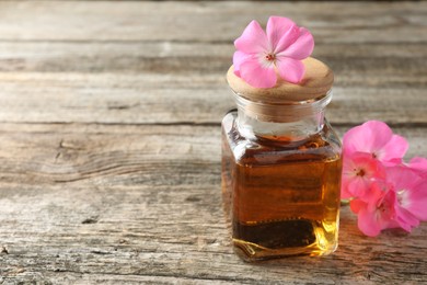 Photo of Bottle of geranium essential oil and beautiful flowers on wooden table, closeup. Space for text