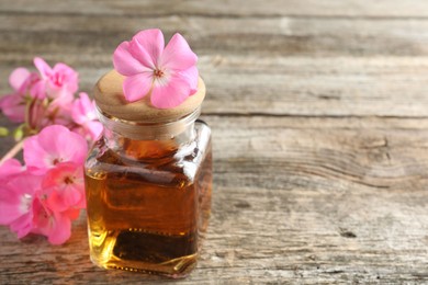 Photo of Bottle of geranium essential oil and beautiful flowers on wooden table, closeup. Space for text