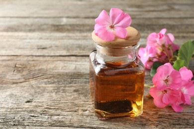 Photo of Bottle of geranium essential oil and beautiful flowers on wooden table, closeup. Space for text