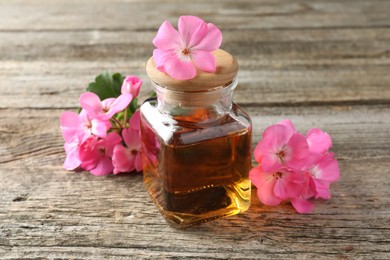 Photo of Bottle of geranium essential oil and beautiful flowers on wooden table, closeup