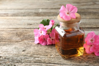 Photo of Bottle of geranium essential oil and beautiful flowers on wooden table, closeup. Space for text