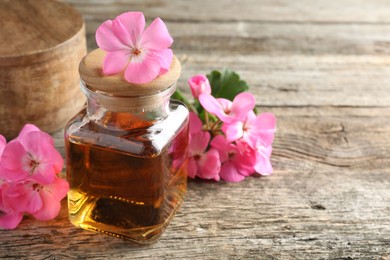 Photo of Bottle of geranium essential oil and beautiful flowers on wooden table, closeup. Space for text