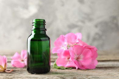 Photo of Bottle of geranium essential oil and beautiful flowers on wooden table, closeup