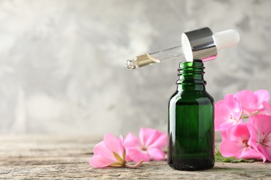 Photo of Geranium essential oil in bottle, pipette and beautiful flowers on wooden table, closeup. Space for text