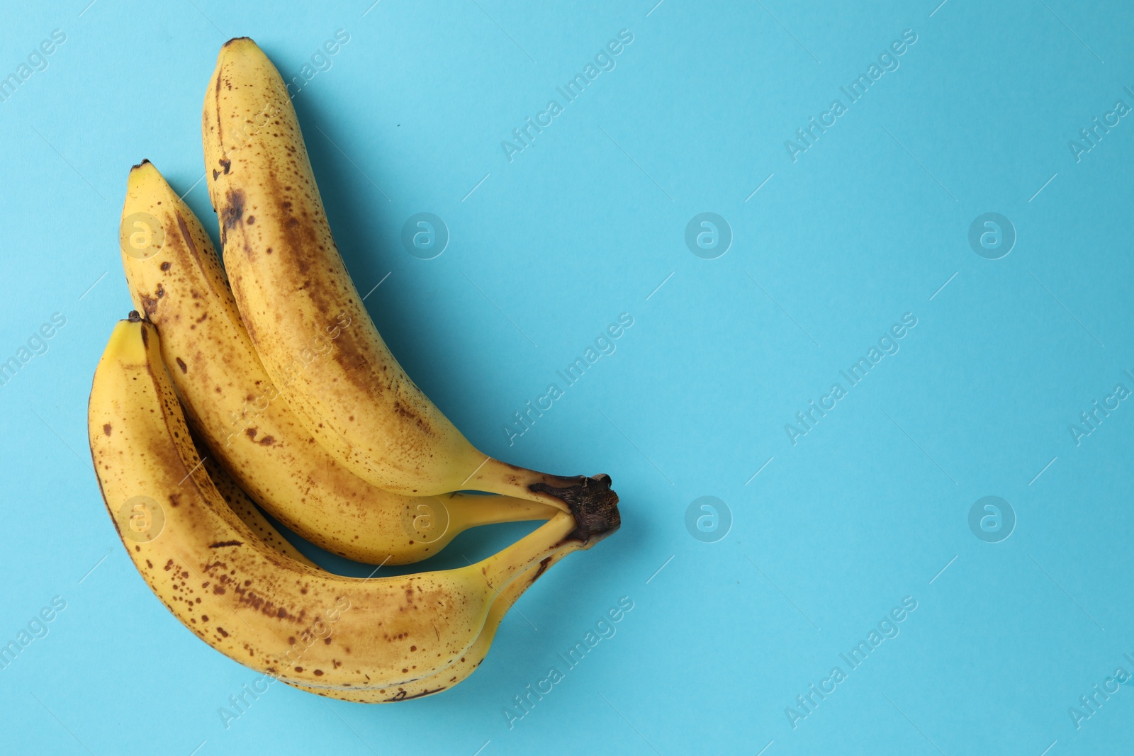 Photo of Bunch of ripe bananas with dark spots on light blue background, top view. Space for text