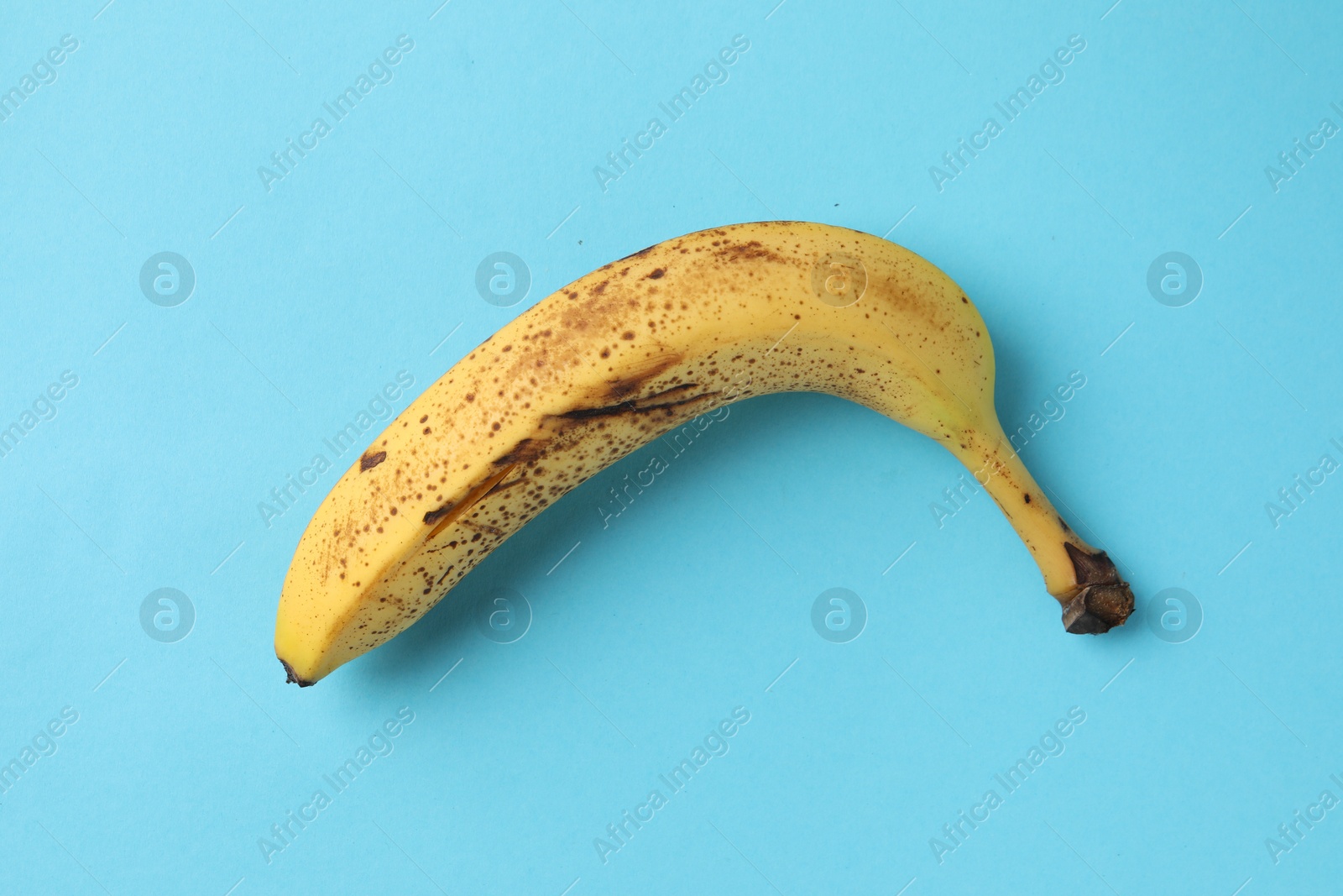 Photo of Ripe banana with dark spots on light blue background, top view