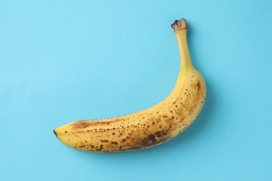 Ripe banana with dark spots on light blue background, top view